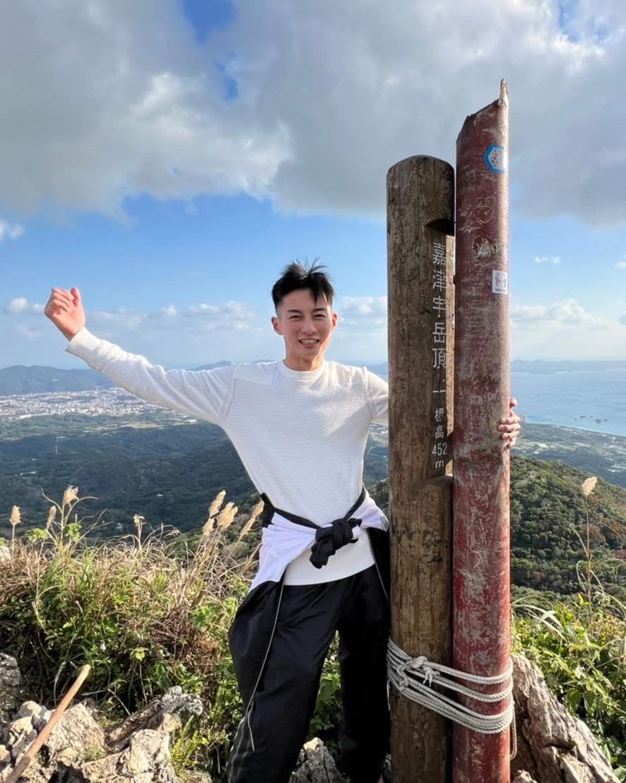 山頂で片手を上げて笑う代表・中根 隆